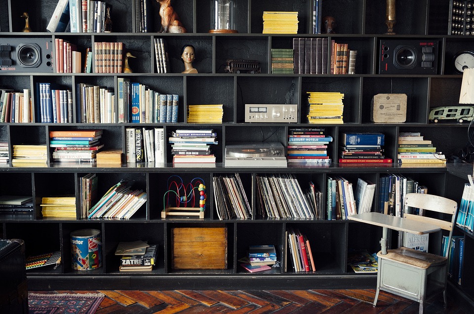 Ein großes, schwarzes Regal gefüllt mit Büchern, Zeitschriften, Schallplatten, Spielzeug und verschiedenen Gegenständen, das eine Mischung aus traditioneller Bibliothek und persönlicher Sammlung darstellt. Symbolbild für eine Library of Things (Bibliothek der Dinge).