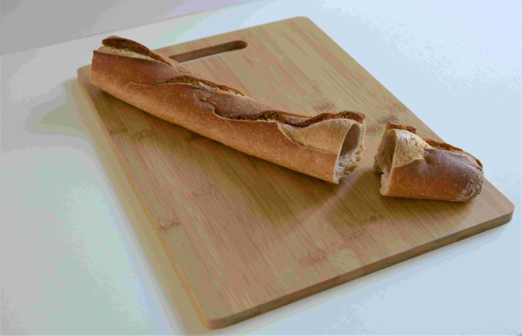 Längliches, angeschnittenes Baguette auf einem Bambusschneidebrett.