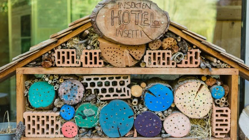 Auf dem Bild ist ein Insektenhotel abgebildet, dass nicht den Kriterien für sinnvolle Insektenhotels entspricht. Das Hotel ist mit bunt angemalten Holzstücken und groben Lochziegeln gefüllt.