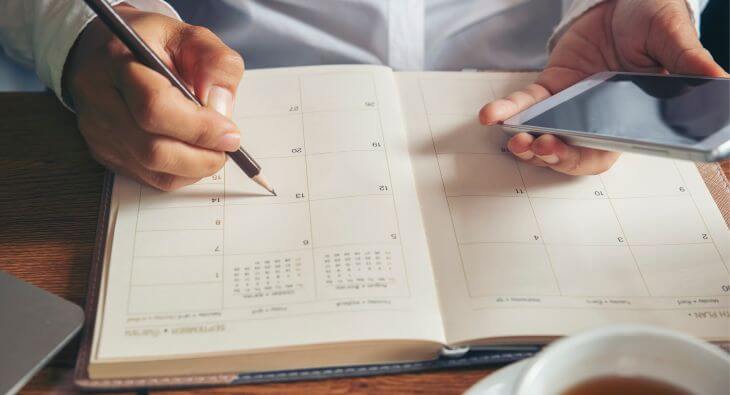 Eine Person trägt etwas mit einem Bleistift in einen Kalender ein.