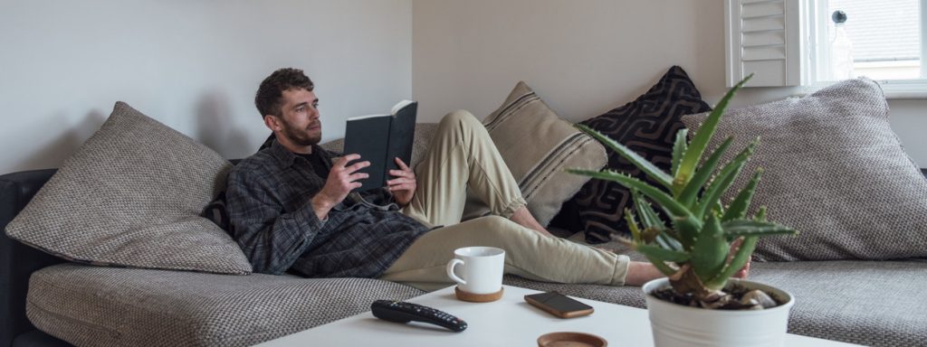 Ein Mann liest entspannt ein Buch auf dem Sofa.